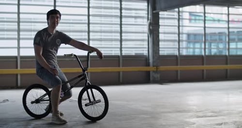 Male Professional BMX Rider Sitting on Bike in Parking Lot