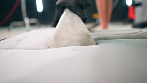 A close-up of a car wash worker using a vacuum cleaner to clean white car seats of detangling