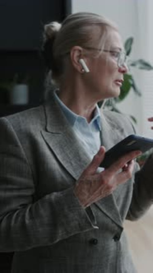 Senior Female CEO Speaking on Phone with Earbuds in Office