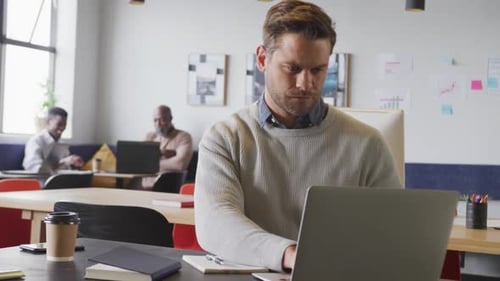 Happy caucasian businessman sitting at table and using laptop at office