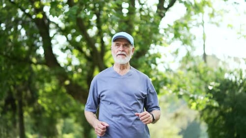 Senior active gray-haired bearded runner jogging in an urban city park. Mature old fitness male