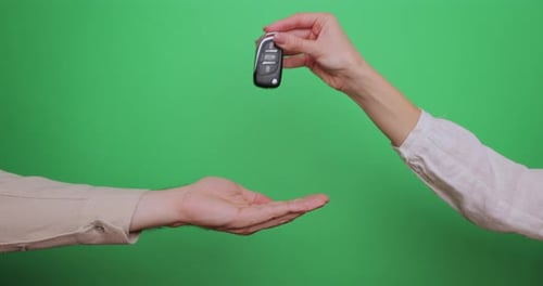 Famale Hand Gives a Car Keys to Male Hand on the Green Background Close Up