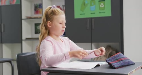 Video portrait of caucasian schoolgirl sitting at desk in school class, with copy space