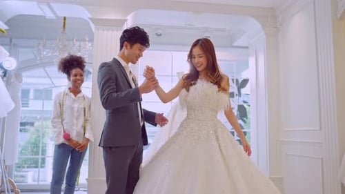 Asian beautiful bride trying on wedding gown with her fiance in studio.