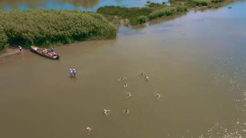 Aerial drone view of a moored boat near the coast of river. Women swimming in river and transparent