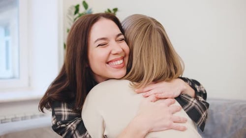 Two Smiling Women Embrace Affectionately Indoors During Daytime