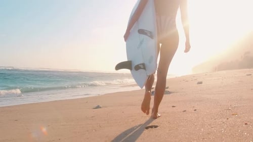 Rückansicht Beine Frau spaziert mit Surfbrett entlang der sandigen Küste des Ozeans