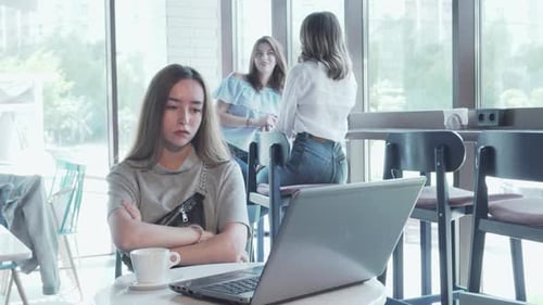 Young Woman Feeling Overwhelmed While Working on Her Laptop in a Bustling Coffee Shop