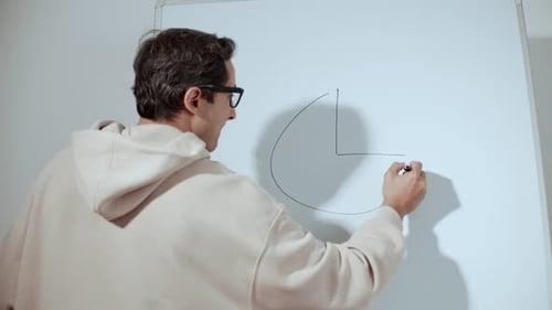 An Adult Man in Glasses and Casual Clothes Draws a Pie Chart on the Board Modern Mentor and Coach