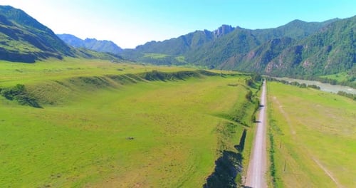 Carretera aérea rural de montaña y pradera en una soleada mañana de verano, carretera asfaltada y río