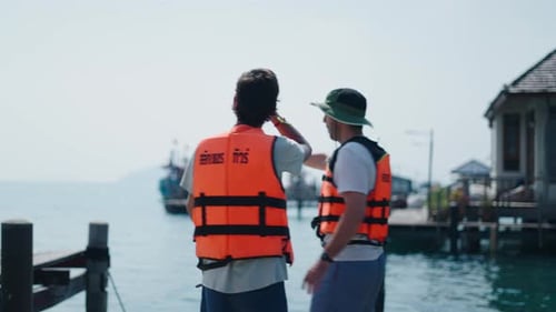 Two Young Men in Life Jackets Discussing Kayaking Routes on a Lakeside Pier