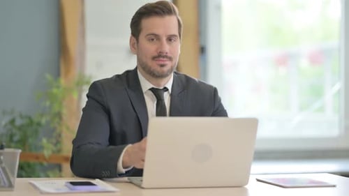 Man in Suit Giving Thumbs Up at Desk