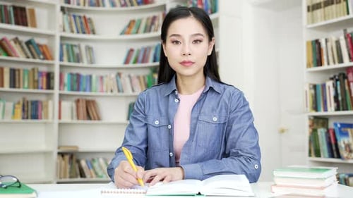 Portrait of asian female student studying taking notes while sitting at desk in campus library space