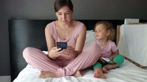 Mother and Daughter Using Smartphones on Hotel Bed