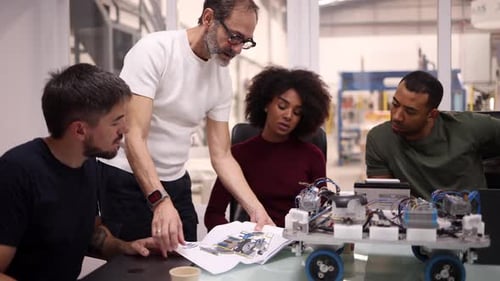 Multi generation and multiracial team of engineers examining a blueprint and working on a robotics p