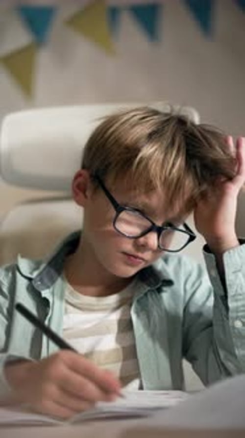 Boy in Glasses Touches Hair on His Head While Doing Exercises in His Notebook