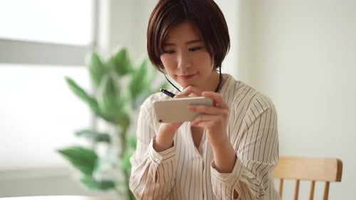 Woman Using Smartphone and Writing at Table