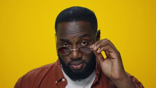 Man Smiling and Adjusting Glasses Against Yellow Background