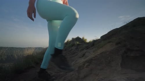 Young fit woman walking up on summit of Mount Batur at sunrise raising arms into air