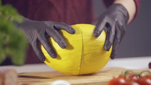 Koch halbiert eine frische gelbe Melone auf einem rustikalen Schneidebrett