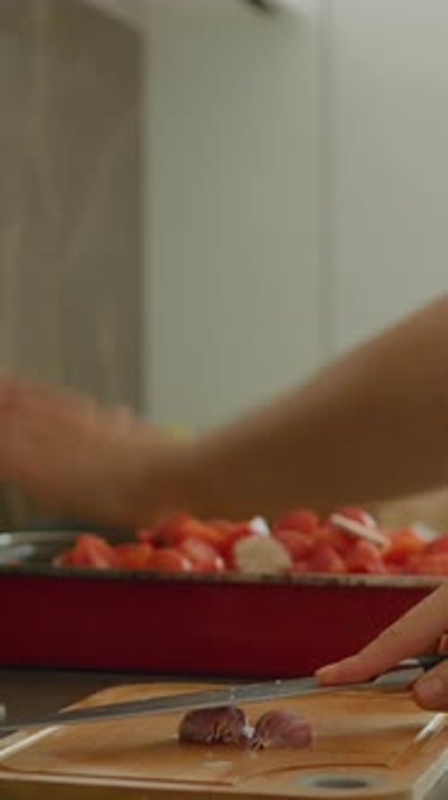 Vertical video Woman crushes garlic on a chopping board in a bright kitchen setting