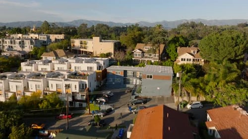 Low Flight Over Residential Houses Lit By Bright Sunshine Revealing Green Vegetation in Public Park