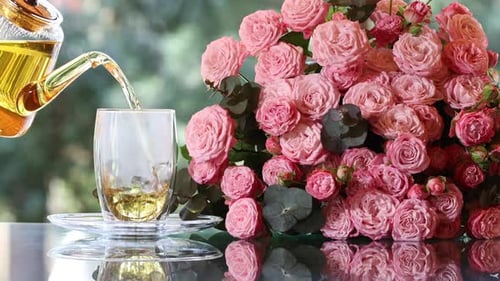 Tea Pouring into Glass Next to Bouquet of Roses