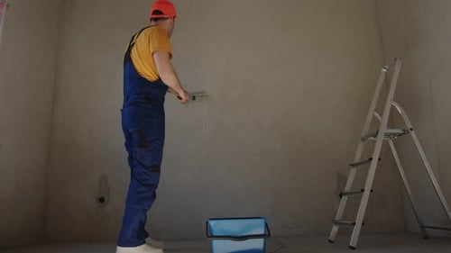 Worker Priming Interior Walls Using a Paint Roller in a Residential Space During Renovation Project