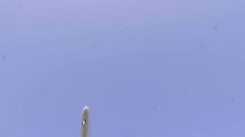 A overhead view of a white passenger airplane on a blue sky background. Bottom view a few seconds be