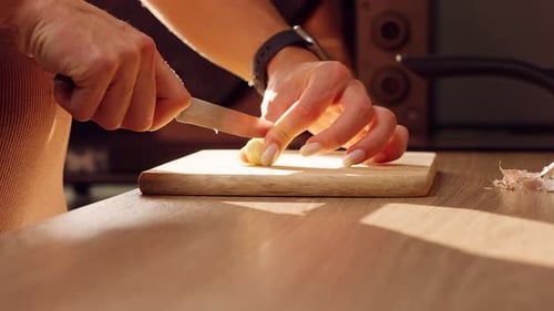 Female Hands Slicing Garlic Clove With Kitchen Knife On Wooden Cutting Board, Fresh Ingredient