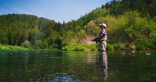 Fly fishing. Angler stands in the river and casts the fly. Fisherman fishing on fly on the river