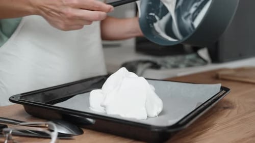 The pastry chef is piping meringue onto a baking sheet covered with parchment paper, in a close-up