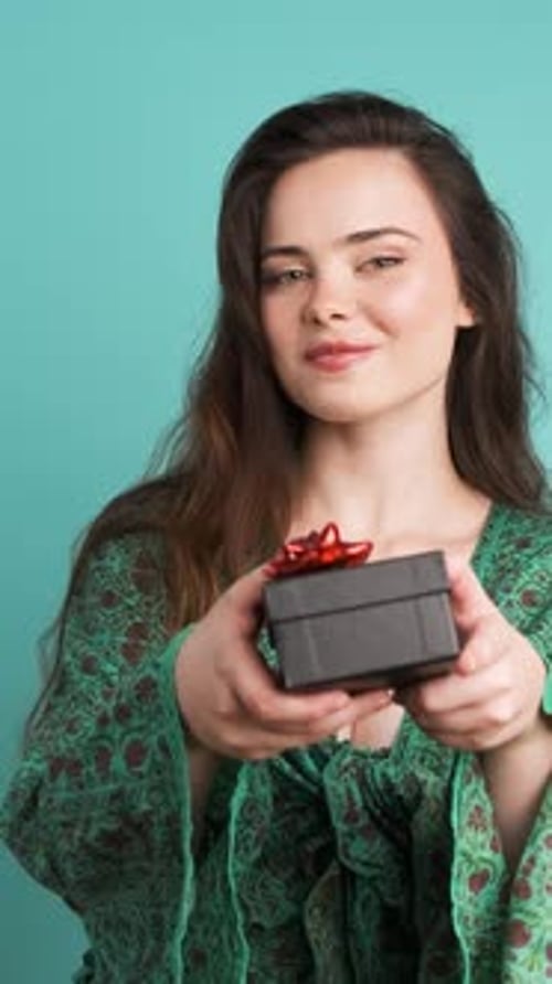 Happy Woman Giving Gift Box and Looking at Camera in Blue Studio