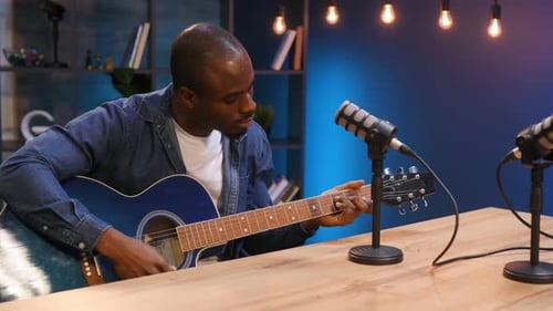Playing acoustic guitar. Man is doing podcast in the studio.