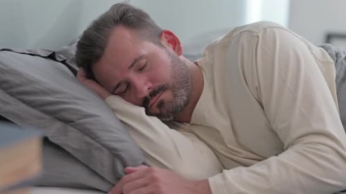 Müder Mann mittleren Alters schläft, während er auf der Seite im Bett liegt