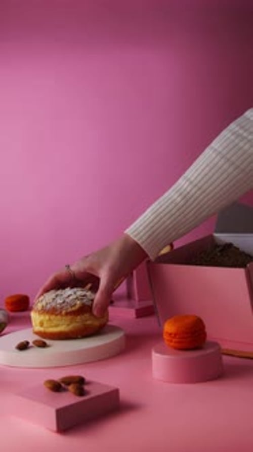 Hand Placing Donut on Table with Pink Background