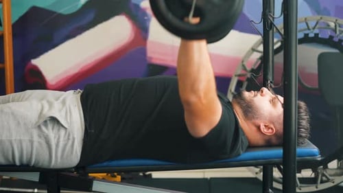 Vue latérale d'un jeune homme faisant un entraînement de développé couché avec une barre dans la salle de sport, un trampolin