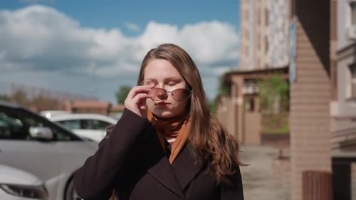 Woman Adjusts Sunglasses Meets Camera Gaze on Urban Street