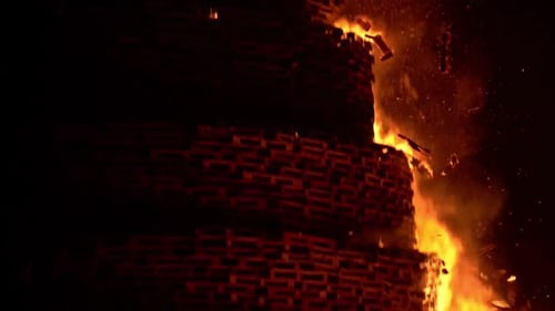 A huge celebration bonfire in Belfast. Bonfire collapses. People watch on and celebrate by dancing a