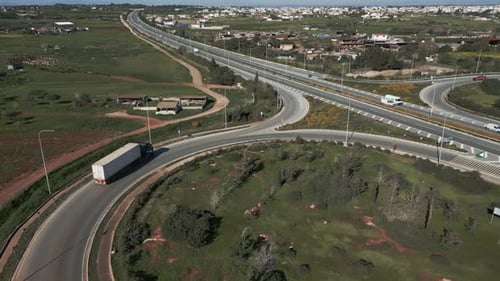 Truck moves along a road near a field in a rural area with vehicles traveling at different speeds