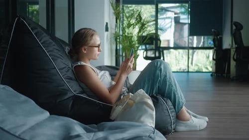 Young Woman Employee is Taking Break From Work Seated on Beanbag Chair in Modern Office Space