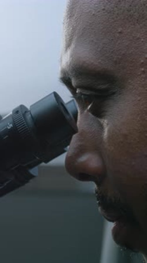Man Looks Through Microscope in Laboratory Setting