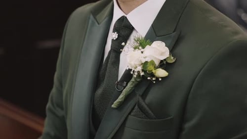 Groom in green suit with white boutonniere, exuding elegance and ready for wedding ceremony.