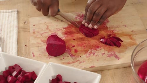 Hands entering frame placing beet upright on counter, African man dicing with knife, filling bowls