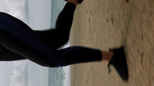 Close up of woman legs in sneakers jogging along sandy seashore. Vertical video