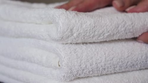 Close-up of hands placing white bath towels on the bed sheet. Concept of room cleaning service.