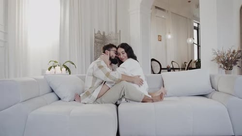 A Man and Woman Sit on a White Couch Smiling in a Comfortable Living Room