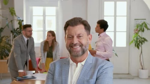 Portrait of smiling businessman in office with his colleagues in background.