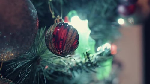 Glittery Balls Hanging On Christmas Tree With Illuminated Festive Lights At Night. - close up