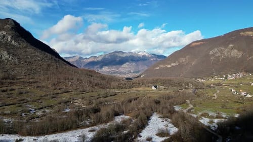 Un Drone survole une vallée enneigée entourée d'arbres et de grandes montagnes